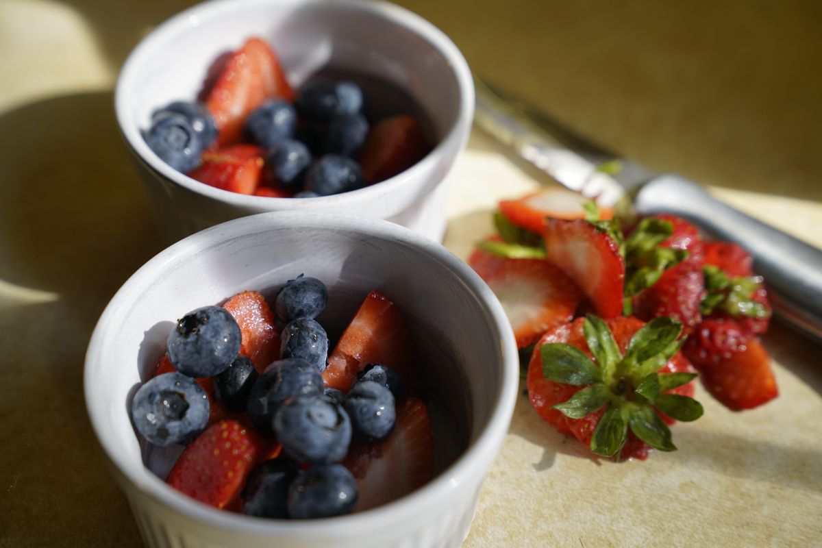 From above of appetizing healthy strawberries and blueberries served in white ceramic bowls and placed on table in kitchen in sunlight